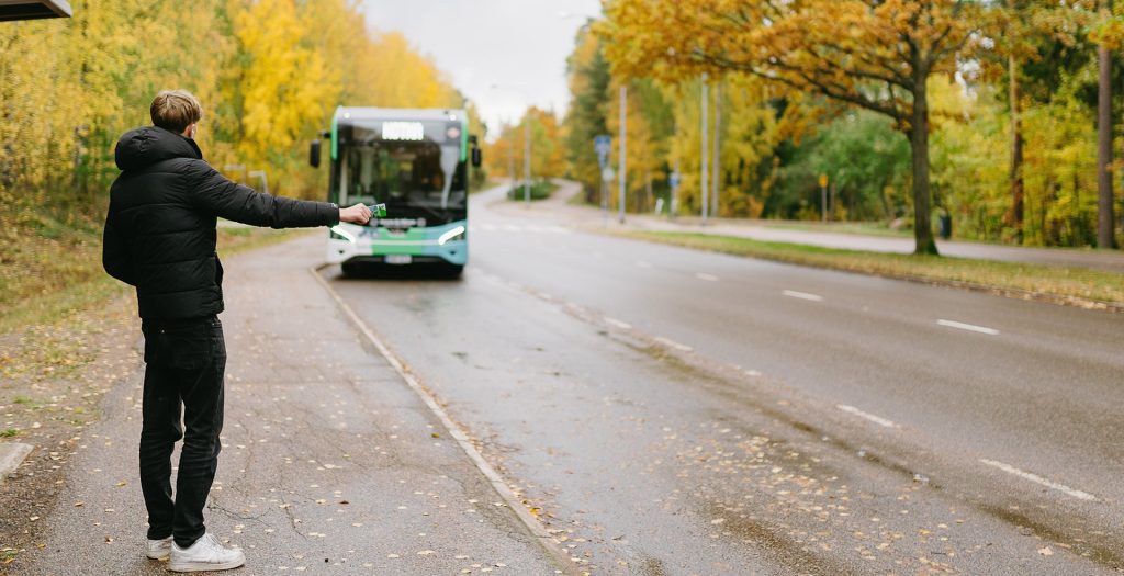 poika viittoo bussia pysähtymään pysäkille syksyisessä maisemassa
