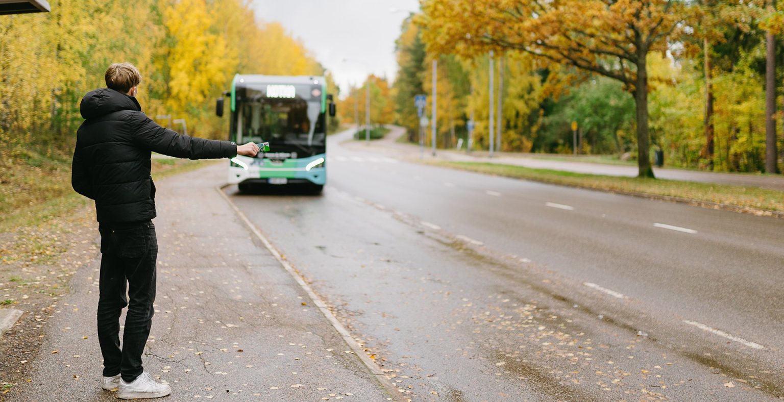 poika viittoo bussia pysähtymään pysäkille syksyisessä maisemassa